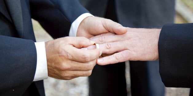 One groom placing the ring on another man's finger during gay wedding.