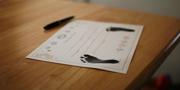 Blank birth certificate has been stamped with baby's footprints. It sits on a table with a pen, ready to be filled in.