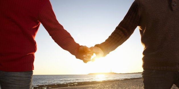 sunlight on hands of gay male couple spending leisure time together walking along the beach