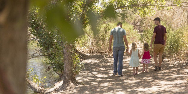 Rear view of male couple strolling with two daughters in park