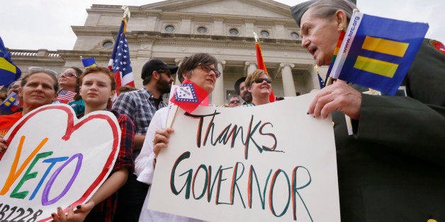 Kristen Hooper, center, and Robert Loyd, right, hold a sign on the steps of the Arkansas state Capitol thanking Arkansas Gov.