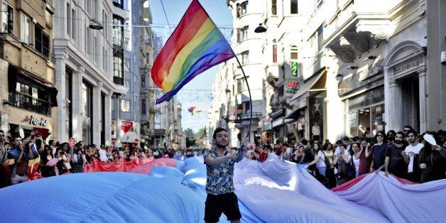 A man waves the gay rainbow flag as he stands on a giant transgender flag during Trans Pride march along Istikbal Avenue in Istanbul, on June 21, 2015. AFP PHOTO / OZAN KOSE (Photo credit should read OZAN KOSE/AFP/Getty Images)