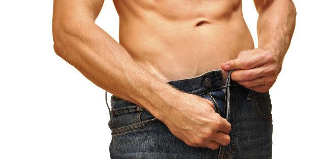 Sexy man with lean abdominals unzips his jeans on white background