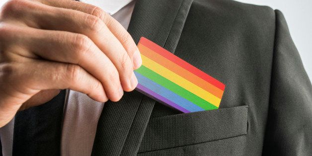 Man withdrawing a wooden card painted as the gay pride flag from his suit pocket, close up of his hand.