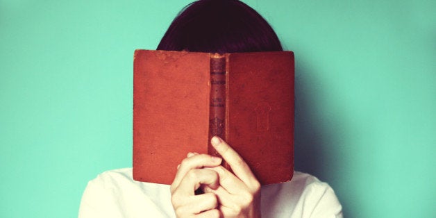 Woman's holding a book in front of her face.