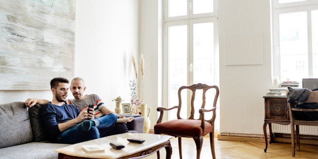 Gay couple sitting on a sofa in their apartment and spending some time together. Wide angle shot.