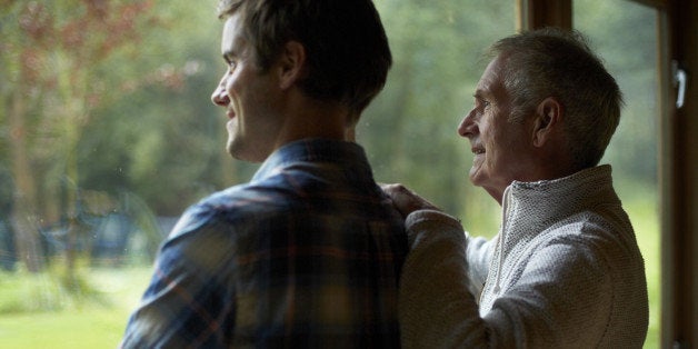 Thoughtful father and son looking through window in cottage