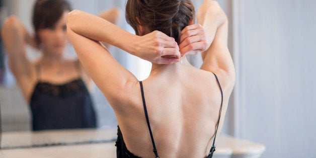 Woman putting on necklace in front of mirror