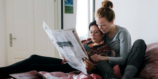 Lesbian couple spending time together and reading newspaper in their bed