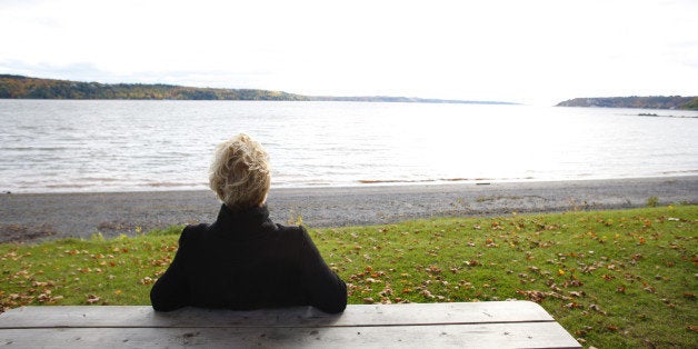 Mature woman sitting at picnic table overlooking river and autumn colors, rear view. 