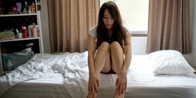 Beautiful girl sitting pensively holding her legs in bedroom.