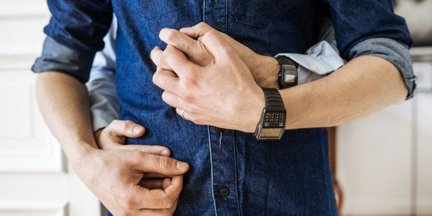 Close up shot of hands of a gay couple hugging. Focus on their hands in front of their body.