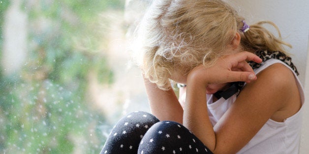 lonely blond girl sitting by the window with head in hands and crying