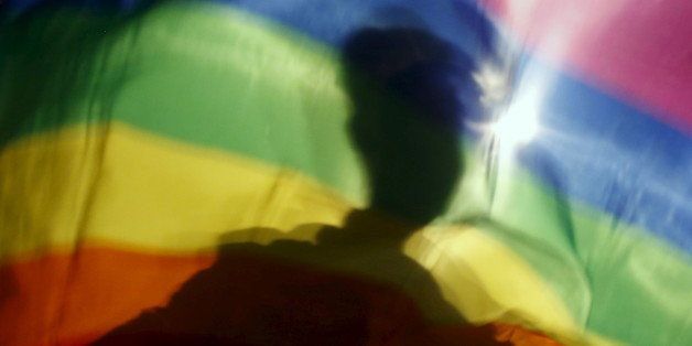 A gay man is silhoutted on a gay rainbow flag during a demonstration for gay rights in Hanoi, Vietnam, November 24, 2015. While transgender, gay and lesbian people are persecuted and even jailed in many Asian countries, Vietnam has quietly become a trailblazer, with laws to decriminalize gay marriage and co-habitation and recognize sex changes on identity documents. Picture taken November 24, 2015. REUTERS/Kham