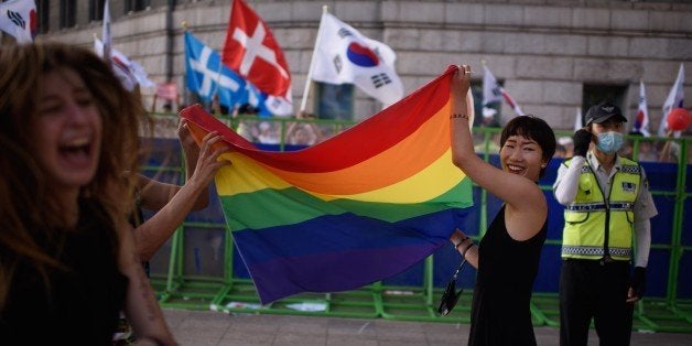 Participants of a gay pride march wave a rainbow flag as they stand before a police cordon set up to keep out anti-gay Christian activists, in Seoul on June 28, 2015. Thousands of participants of South Korea's annual gay pride parade marched across central Seoul, with many celebrating the US Supreme Court's historic decision allowing same-sex couples to wed. Gay and transgender Koreans live largely under the radar in a country that remains deeply conservative about matters of sexual identity and where many still regard homosexuality as a foreign phenomenon. Thousands of Christian activists stood behind police barriers to wave banners and chant slogans at those taking part, condemning what they called an attempt to turn the South Korean capital into 'Sodom and Gomorrah.' AFP PHOTO / Ed Jones (Photo credit should read ED JONES/AFP/Getty Images)