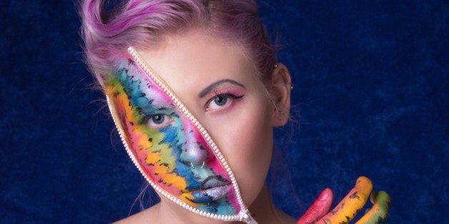 Vertical colour studio shot of young woman with pink hair in 40s style and zippers on face and hand. Zippers are open to show