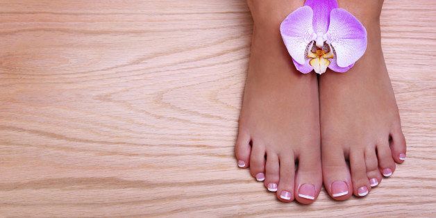 Pedicure with pink orchid flower on wooden background. Beautiful female feet with french manicure. Foot care. Spa