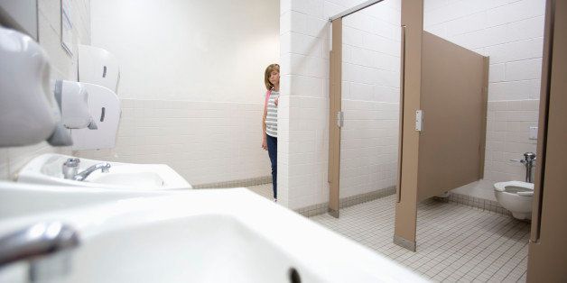 Eleven-year-old girl peeks around corner of bathroom wall while entering.