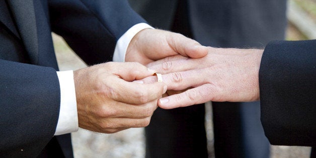 One groom placing the ring on another man's finger during gay wedding.