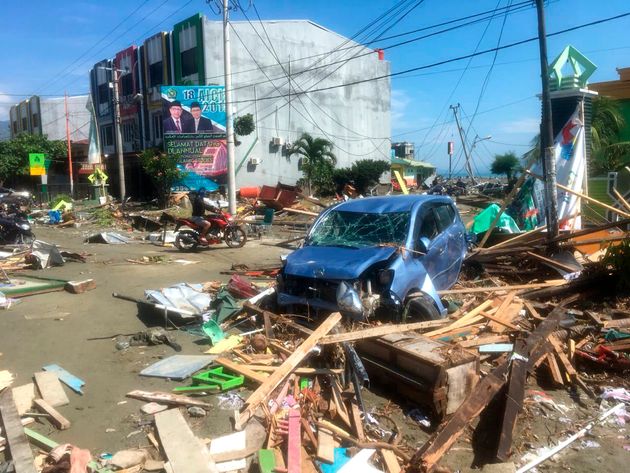 A motorbike passes the wreckage of a car in Palu.