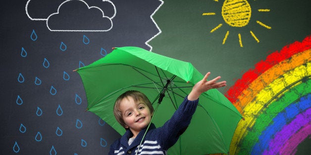 Child holding an umbrella standing in front of a chalk drawing of changing weather from rain storm to sun shine with a rainbo