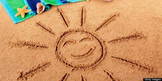 Beach background with smiling sun drawn in the sand. Sharp focus on the sun with background objects slightly blurred. Studio