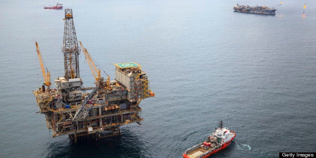 Aerial photo of an offshore oil field with a large fixed oil rig, two FPSO vessels, and numerous support and supply vessels of various sizes. 