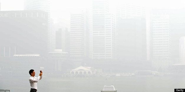 A man takes pictures of buildings blanketed by haze in Singapore on June 19, 2013. Singapore's Pollutant Standards Index again shot above the 'unhealthy' threshold of 152. AFP PHOTO/Roslan Rahman (Photo credit should read ROSLAN RAHMAN/AFP/Getty Images)