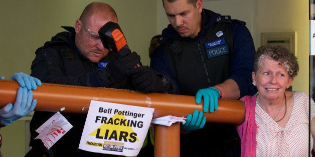A police officer uses a tool to cut through a pipe glued to the arm of a protester forming a makeshift barrier as climate pro