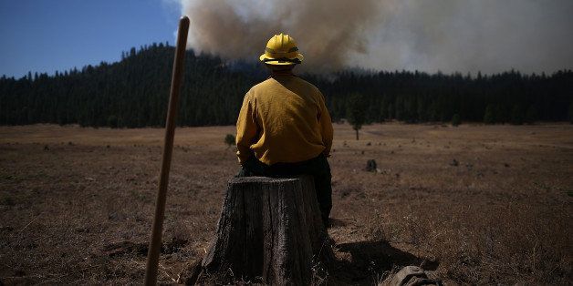 GROVELAND, CA - AUGUST 25: U.S. Fish and Wildlife Service firefighter Corey Adams sits on a tree stump as he monitors the Rim Fire on August 25, 2013 near Groveland, California. The Rim Fire continues to burn out of control and threatens 4,500 homes outside of Yosemite National Park. Over 2,000 firefighters are battling the blaze that has entered a section of Yosemite National Park and is currently 7 percent contained. (Photo by Justin Sullivan/Getty Images)