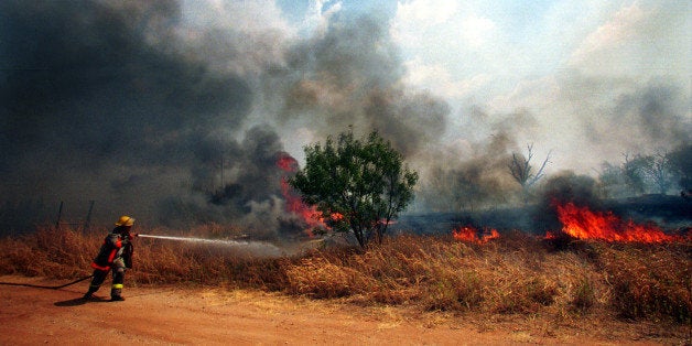377913 01: A firefighter sprays water on a fast moving grass fire, September 7, 2000 in Ranger, Texas. Forest fires and grass