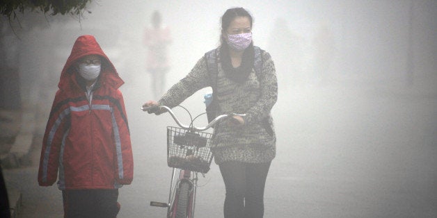 A woman walks with her child on a street as schools were closed due to the heavy smog in Jilin, northeast China's Jilin province on October 22, 2013. Thick smog enveloped China's northeast area for a third day on October 22. CHINA OUT AFP PHOTO (Photo credit should read STR/AFP/Getty Images)