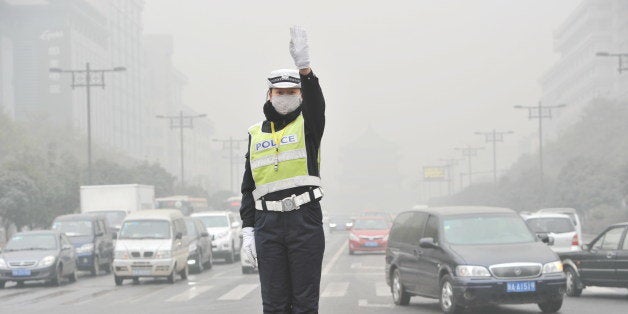 XI AN, CHINA - DECEMBER 18: (CHINA OUT) A traffic policewoman wearing mask directs traffic as heavy smog engulfs the city on