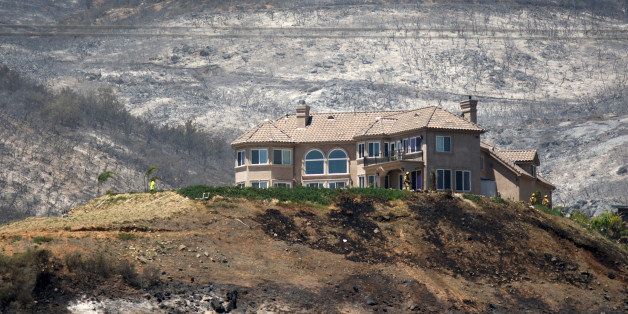 SAN MARCOS, CA - MAY 16: Scorched hills surround firefighters and a hilltop house after it saved from the Cocos fire on May 16, 2014 in San Marcos, California. The fire continues to threaten communities with little containment three days after nine wildfires broke out in a single day in San Diego County. (Photo by David McNew/Getty Images)