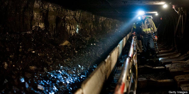A coal miner shines his head lamp on coal transported on a conveyor belt after being sheared off the wall during longwall min