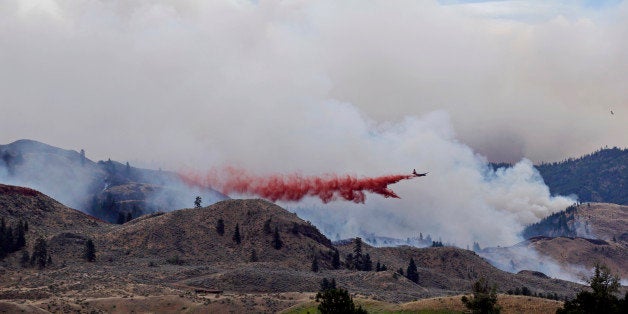 A plane drops fire retardant over a wildfire as clouds of smoke billow behind and above Saturday, July 19, 2014, near Carlton, Wash. A wind-driven, lightning-caused wildfire racing through rural north-central Washington destroyed about 100 homes Thursday and Friday, leaving behind solitary brick chimneys and burned-out automobiles as it blackened hundreds of square miles in the scenic Methow Valley northeast of Seattle. (AP Photo/Elaine Thompson)