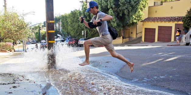 A man leaps over water flooding a side street after a water main break sent churning, muddy water down Sunset Boulevard and hilly side streets on the famed Sunset Strip in West Hollywood, Calif., Friday, Sept. 26, 2014. The Los Angeles Department of Water and Power said the break occurred in a 36-inch steel, riveted pipe that was constructed in 1916. No injuries were reported. (AP Photo/Nick Ut)