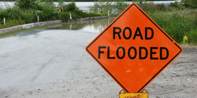 Orange caution sign saying road flooded against Fraser river flooding over road.