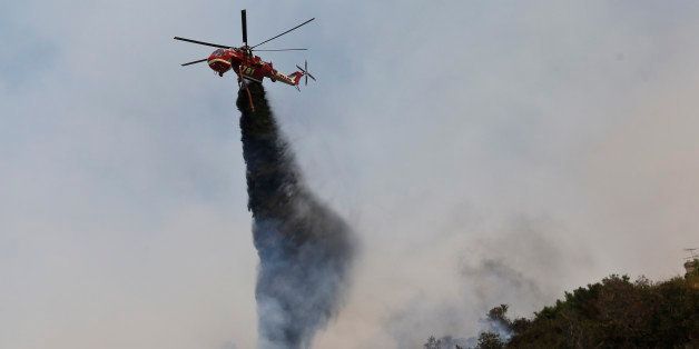 FILE - This May 15, 2014 file photo shows a helicopter dropping retardants while battling the Cocos fire in San Marcos, Calif. A judge ruled Wednesday Aug. 20, 2014, that a 13-year-old is competent to stand trial on allegations she deliberately started this wildfire that destroyed three dozen homes north of San Diego in May. (AP Photo/Lenny Ignelzi)