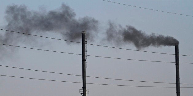 An Indian man works on the roof of a factory as smoke rises from another factory at an industrial area in Ahmadabad, India, Friday, Dec. 5, 2014. India says it is taking bold steps against climate change with plans for a five-fold increase in renewable energy capacity. However, Environment Minister Prakash Javadekar said the country won't act to curb carbon emissions because it first must pursue economic growth to eradicate poverty. (AP Photo/Ajit Solanki)