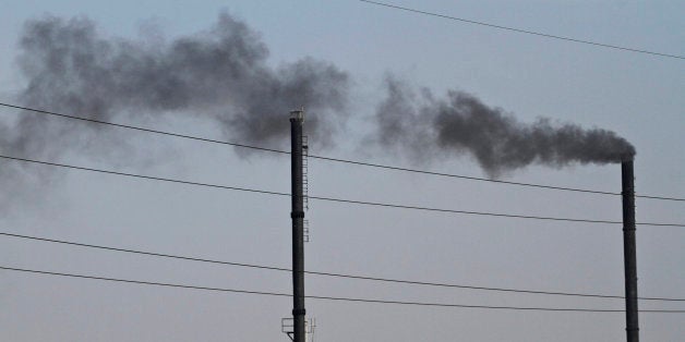 An Indian man works on the roof of a factory as smoke rises from another factory at an industrial area in Ahmadabad, India, F