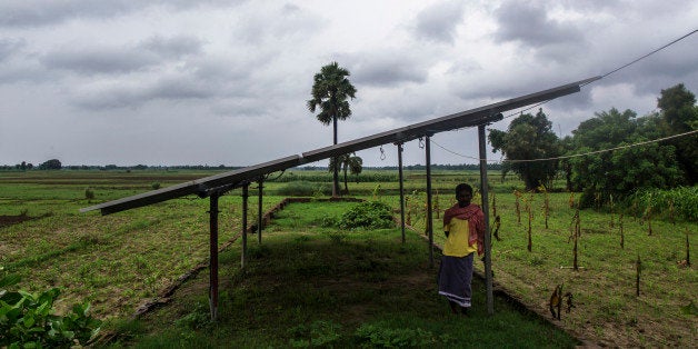 A man stands under solar panels, part of a solar power microgrid owned and operated by Veddis Solars Pvt., in the village of