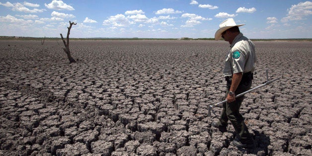 FILE - In this Wednesday, Aug. 3, 2011 file photo, Texas State Park police officer Thomas Bigham walks across the cracked lake bed of O.C. Fisher Lake in San Angelo, Texas. A combination of the long periods of 100-plus degree days and the lack of rain in the drought-stricken region has dried up the lake that once spanned over 5400 acres. The year 2011 brought a record heat wave to Texas, massive floods in Bangkok and an unusually warm November in England. How much has global warming boosted the chances of events like that? Quite a lot in Texas and England, but apparently not at all in Bangkok, according to new analyses released Tuesday, July 10, 2012. Researchers calculated that global warming has made such a Texas heat wave about 20 times more likely to happen during a La Nina year. (AP Photo/Tony Gutierrez)