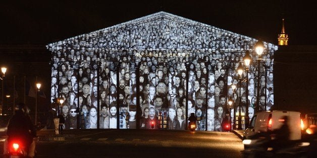 A picture taken on November 30, 2015 shows images of more than 500 people being projected onto the facade of the French National Assembly building during the 2015 UN Climate Change Conference (COP21) in Paris. The Standing March is the collaborative work by the French artist known as JR and US filmmaker Darren Aronofsky. / AFP / Eric Feferberg / RESTRICTED TO EDITORIAL USE - MANDATORY MENTION OF THE ARTIST UPON PUBLICATION (Photo credit should read ERIC FEFERBERG/AFP/Getty Images)