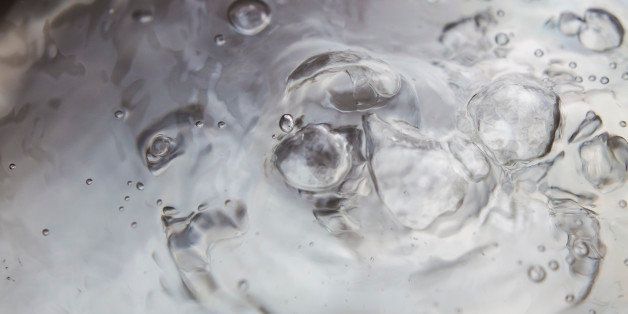 Bubbles boiling transparent hot water on a close up still of a silvered gray pan.