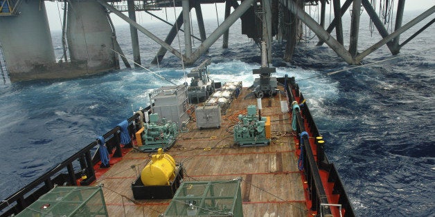 Air guns blast at the stern of a work vessel alongside an offshore oil rig. The air guns are deployed by cranes. Air compress