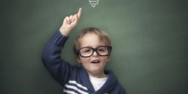 Schoolboy standing in front of a blackboard with a bright idea light bulb above his head concept for innovation, imagination and inspirational ideas