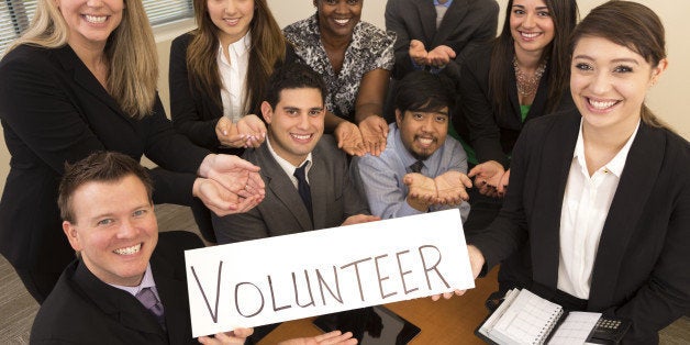 Team of business professionals hold a 'Volunteer' sign with hands cupped to represent the concept of service.