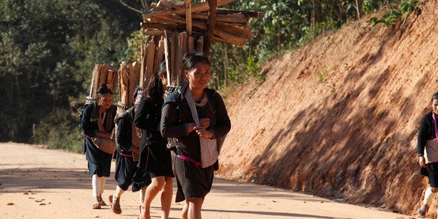 Girls from the Lantan hill tribe carrying wood home along a dust track, wearing traditional dress.