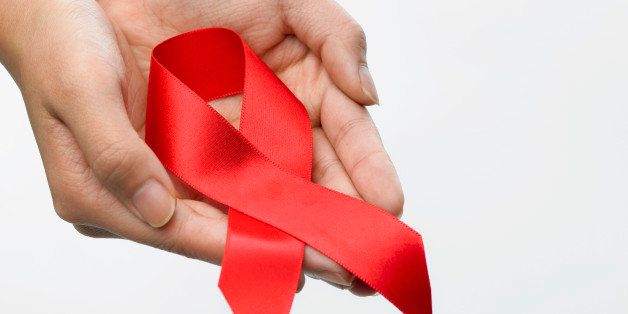Close-up of person's hand holding red ribbon the AIDS symbol